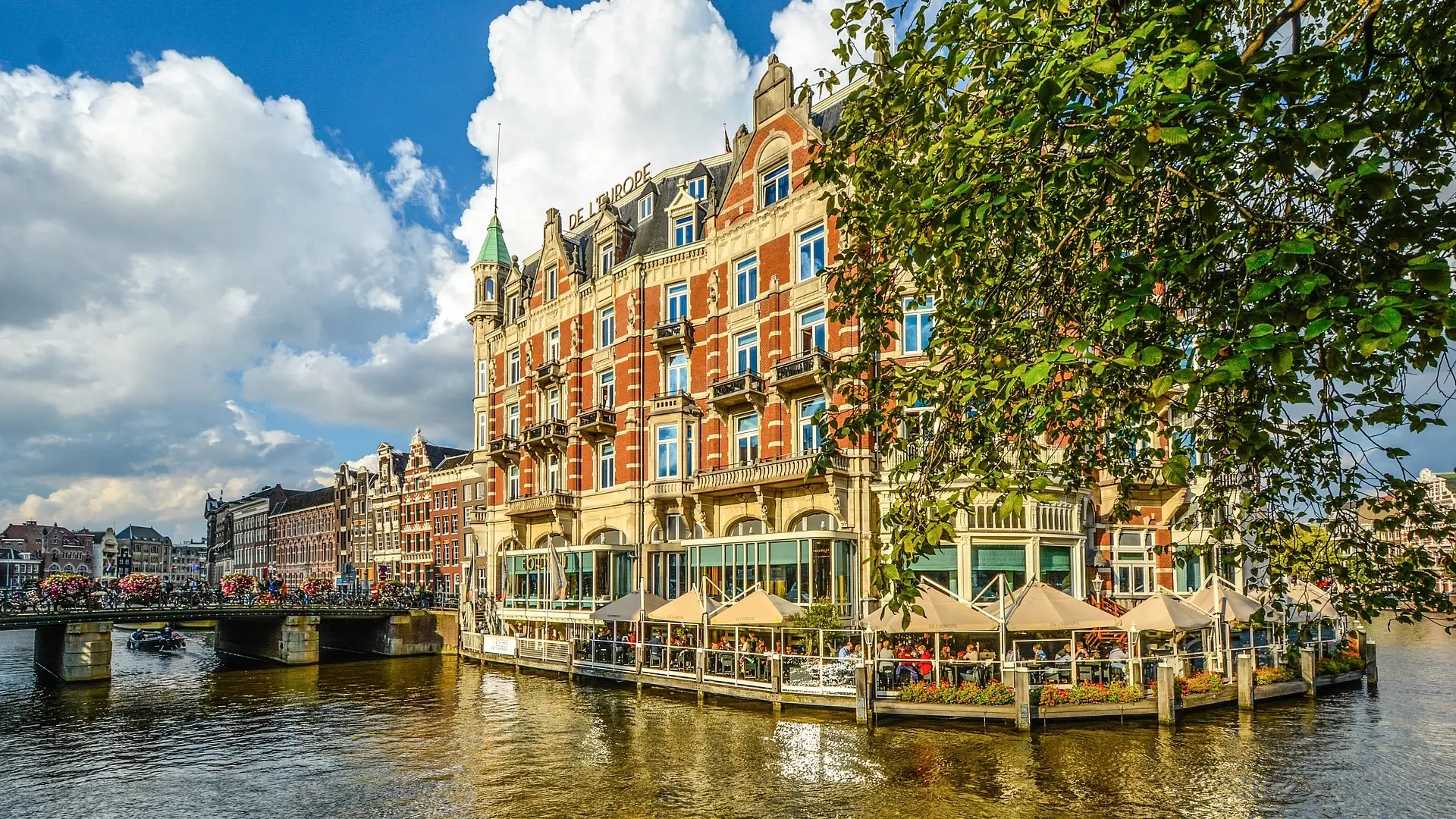 Old school looking building with sign on roof saying: DE L´EUROPE and a bridge with boat going passed in Amsterdam, The Netherlands.