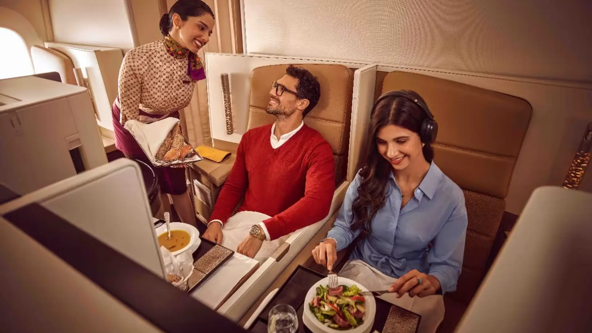 Man with glasses being served bread by a flight attendant while eating soup.