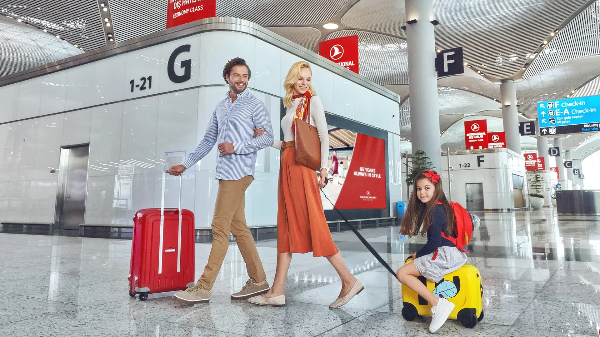 A happy couple and their daughter at the airport ready to check in.