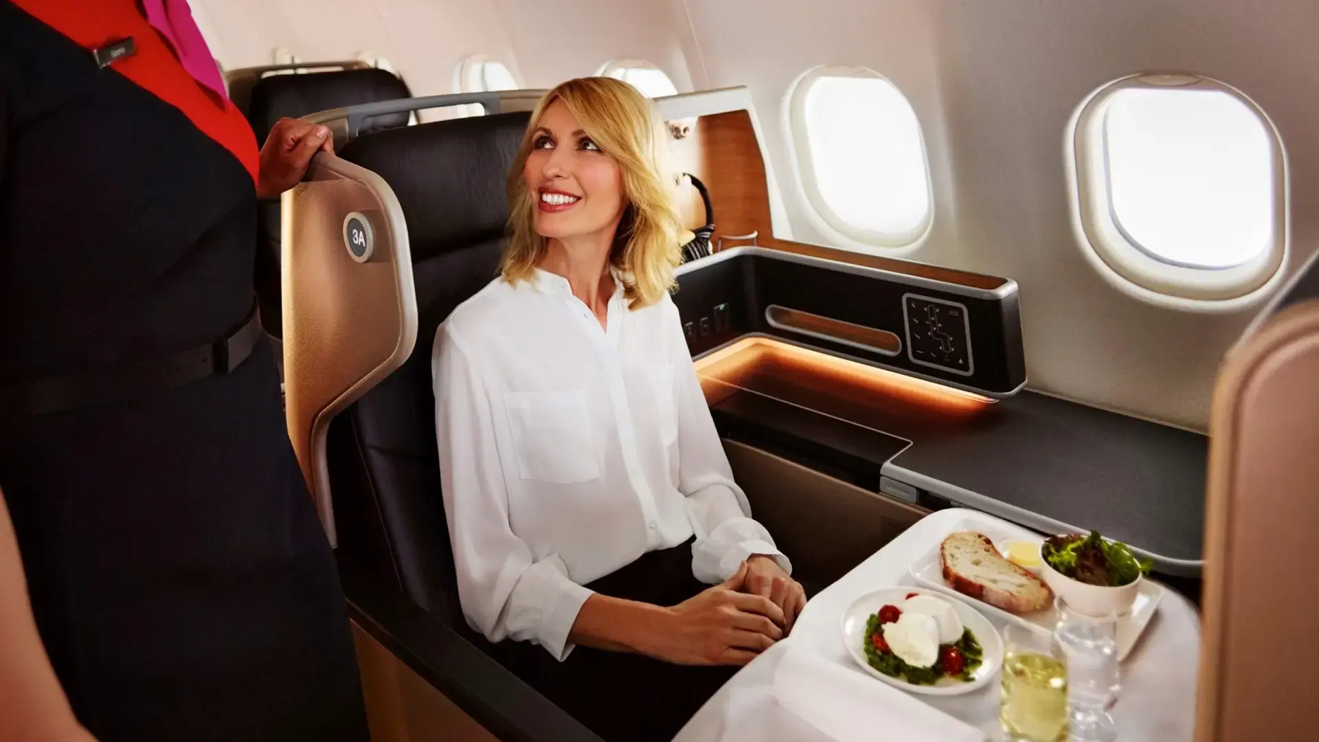 an air hostess speaking to a woman while she is served dinner in Qantas Business Class